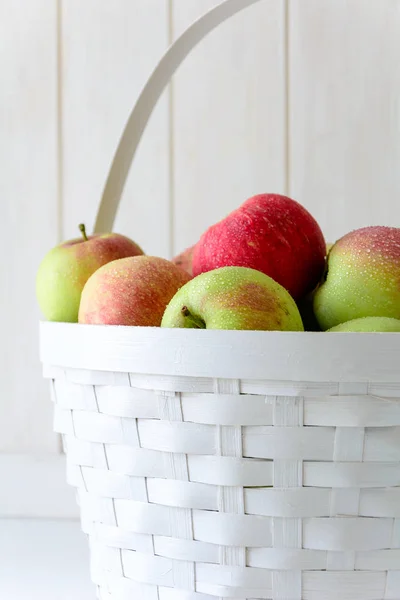 White basket with red and green apples on front of white wooden wall. Harvest concept
