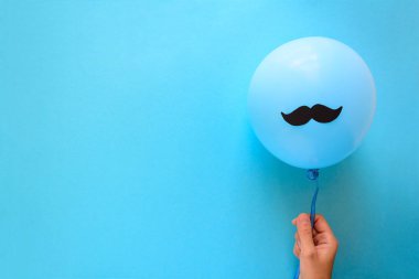 Kağıt bıyıklı mavi balon mavi Kağıt arka plan üzerinde tutan el. Kesip tarzı. Movember