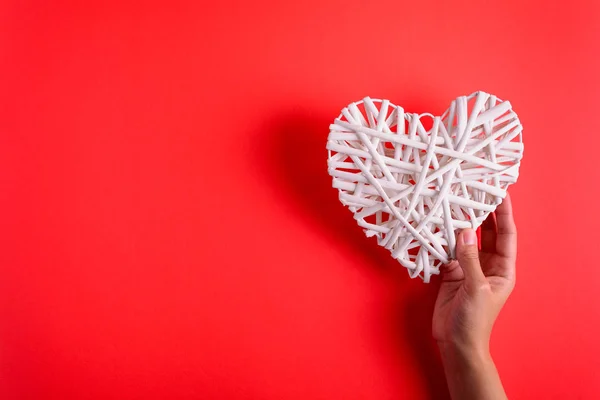 Hands holding white wooden heart on red paper background. Heart health concept. Top view. Flat lay. Copy space