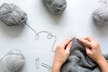 Kız gri kazak örgü iğneleri gri ahşap arka plan üzerinde dokuma kumaşlar. Örgü işlemi. Üstten görünüm. Lay paylamak