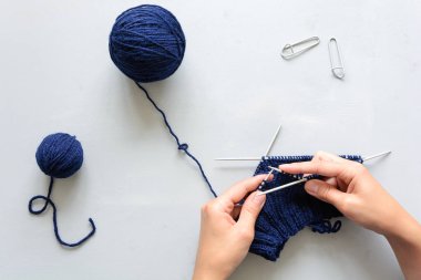 Kız mavi şapka örgü iğneleri gri ahşap arka plan üzerinde dokuma kumaşlar. Örgü işlemi. Üstten görünüm. Düz yatıyordu