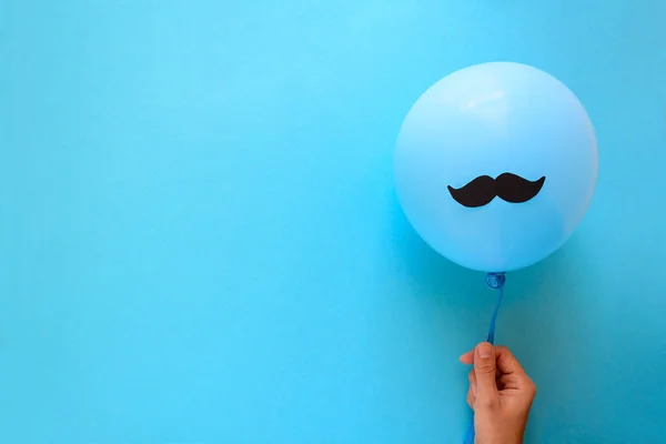Kağıt bıyıklı mavi balon mavi Kağıt arka plan üzerinde tutan el. Kesip tarzı. Movember kavramı. Üstten görünüm. Düz yatıyordu. Kopya alanı