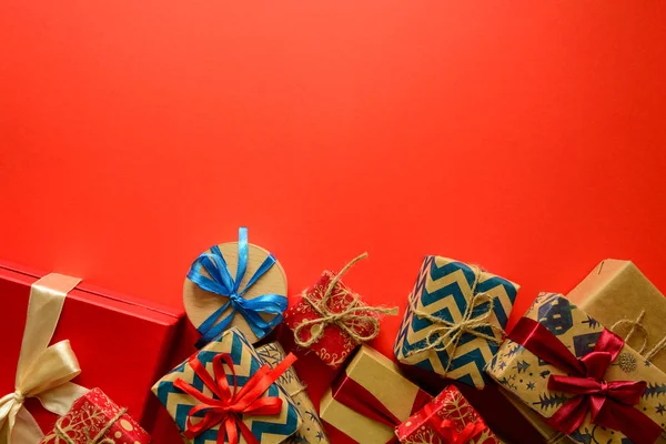 Top view on Christmas gifts wrapped in gift paper decorated with ribbon on red paper background. New Year, holidays and celebration decorations concept. Copy space. Flat lay