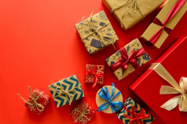 Üstten görünüm Noel hediyeleri üzerinde kırmızı Kağıt arka plan üzerinde kurdele ile süslenmiş hediye kağıt sarılı. Yeni yıl, tatil ve kutlama süslemeleri kavramı. Uzay kopyalayın. Düz yatıyordu