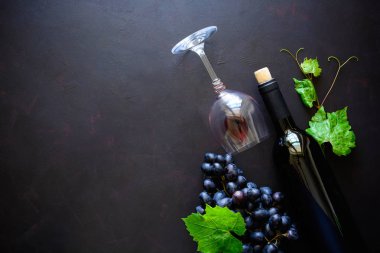 İki kadehlerin kırmızı şarap ile şişe ve üzüm yaprakları koyu ahşap arka plan üzerinde yalan. Üstten görünüm. Düz yatıyordu. Kopya alanı