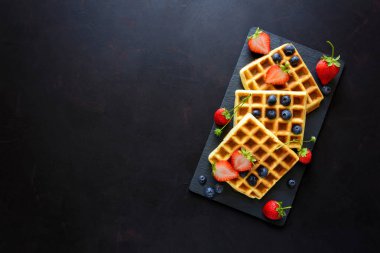 Çilek ve koyu ahşap arka plan üzerinde kayrak plaka üzerinde yaban mersini ile Belçika Waffle. Üstten görünüm. Kopya alanı