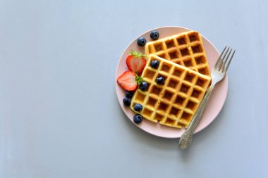 Gri ahşap zemin üzerine pembe plaka üzerinde bir yaban mersini ve çilek ile Belçika Waffle. Üstten görünüm. Kopya alanı