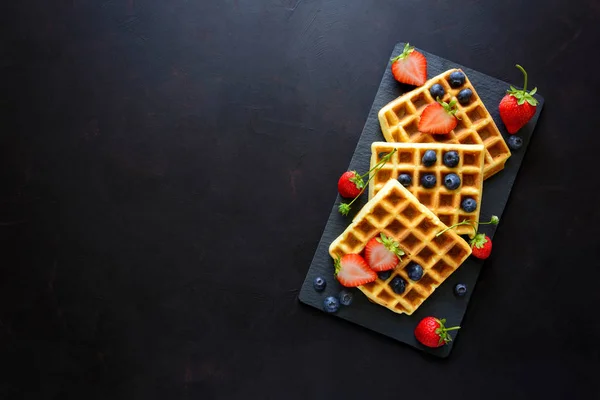 Çilek ve koyu ahşap arka plan üzerinde kayrak plaka üzerinde yaban mersini ile Belçika Waffle. Üstten görünüm. Kopya alanı