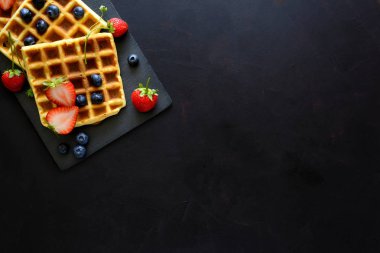 Çilek ve koyu ahşap arka plan üzerinde kayrak plaka üzerinde yaban mersini ile Belçika Waffle. Üstten görünüm. Kopya alanı