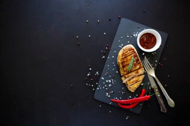 Biberiye, karabiber, ketçap ve koyu ahşap zemin üzerine baharat ile kayrak tabakta tavuk fileto ızgara. Üstten görünüm. Düz yatıyordu. Kopya alanı