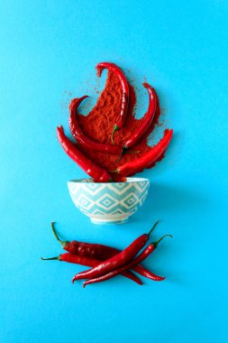 Kağıt arka plan mavi ham Olgun kırmızı biber biber bezelye ve biber tozu yatan şenlik ateşi formunda. Üstten görünüm. Düz yatıyordu