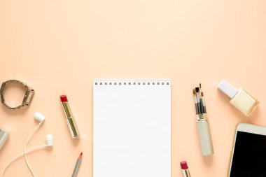 Kadınsı çalışma alanı ile smartphone, kulaklık, defter, kalem, tırnak cilası, saat, fırçalar ve ruj. Düz yatıyordu. Üstten görünüm. Kopya alanı