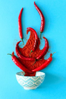 Kağıt arka plan mavi ham Olgun kırmızı biber biber bezelye ve biber tozu yatan şenlik ateşi formunda. Üstten görünüm. Düz yatıyordu