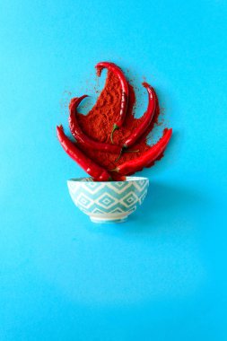 Kağıt arka plan mavi ham Olgun kırmızı biber biber bezelye ve biber tozu yatan şenlik ateşi formunda. Üstten görünüm. Düz yatıyordu