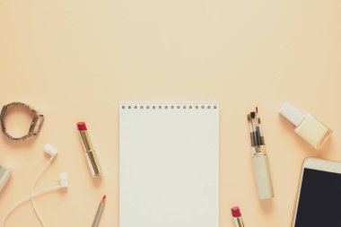 Kadınsı çalışma alanı ile smartphone, kulaklık, defter, kalem, tırnak cilası, saat, fırçalar ve ruj. Düz yatıyordu. Üstten görünüm. Uzay kopyalayın. Tonda