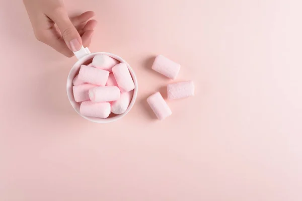 Feminine hands holding hot chocolate with marshmallow candies on pink paper background. Top view. Copy space
