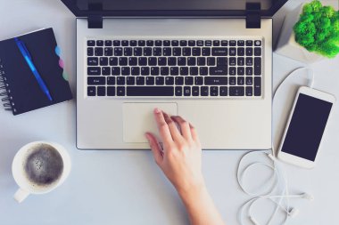 Dizüstü bilgisayar, smartphone, defter, kalem ve kahve ile gri ahşap ofis resepsiyon masası. Erkek bir dizüstü bilgisayar kullanarak ve bir fincan kahve tutan eller. Üstten görünüm. Uzay kopyalayın. Düz yatıyordu. Tonda