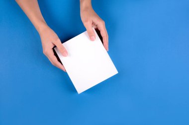 Beyaz holding kadınsı eller mavi Kağıt arka plan üzerinde kutusu hediye. Üstten görünüm. Uzay kopyalayın. Tatil kutlama veya cilt bakım kavramı
