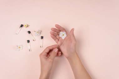 Parfüm örnekleri ve beyaz çiçek, pembe arka plan holding eller. Üstten görünüm. Kopya alanı