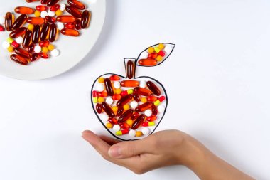 Beyaz arka plan üzerinde renkli kapsül ve hapları ile çizim elma tutan el. Sağlık Hizmetleri (vitaminler) veya sentetik Gıda kavramı. Üstten görünüm