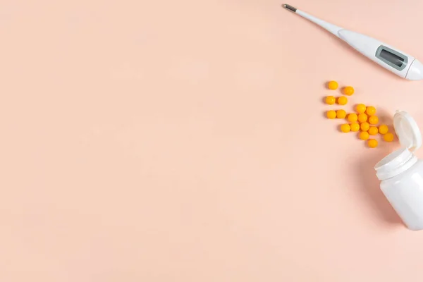 Medical electronic thermometer, drops and pills on pink background. Health care concept. Top view. Copy space. Flat lay