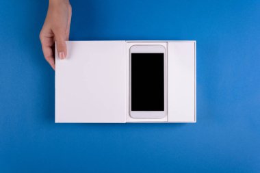 Kağıt arka plan beyaz hediye kutusu ile akıllı telefon holding kadınsı eller mavi. Üstten görünüm. Uzay kopyalayın. Tatil kutlama kavramı