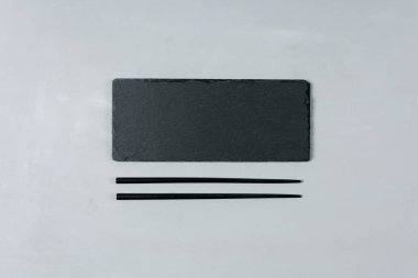 Boş siyah arduvaz levha çubuk üzerinde gri ahşap arka plan ile. Düz yatıyordu. Üstten görünüm. Gıda kavramı