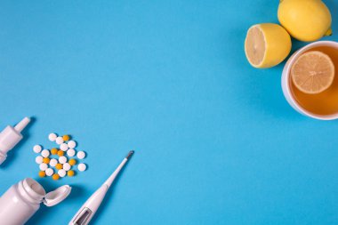 Tıbbi elektronik termometre, hap, burun için sprey ilaç şişesiyle ve mavi arka plan üzerinde limonlu çay. Sağlık kavramı. Bitkisel ve kimyasal ilaç. Üstten görünüm. Uzay kopyalayın. Düz yatıyordu