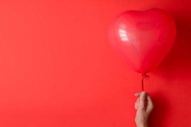 Kırmızı Kağıt arka plan üzerinde kırmızı kalp balonlar tutan el. Sevgililer günü veya Doğum günü kutlama kavramı