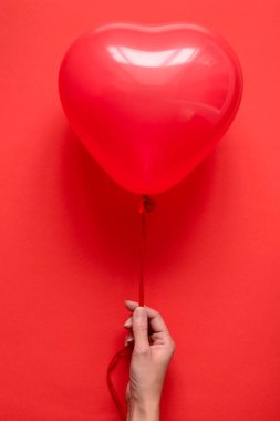 Kırmızı Kağıt arka plan üzerinde kırmızı kalp balonlar tutan el. Sevgililer günü veya Doğum günü kutlama kavramı