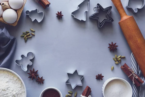 Cooking Christmas cookies. Ingredients for gingerbread dough: flour, eggs, sugar, cocoa, cinnamon sticks, anise stars and cookie cutters on gray wooden background. Flat lay. Top view. Copy space. Toned