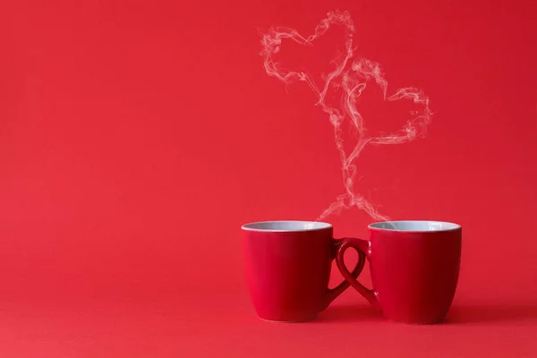 Cups of tea or coffee with steam in two heart shape on red background. Valentine's day celebration or love concept. Copy space