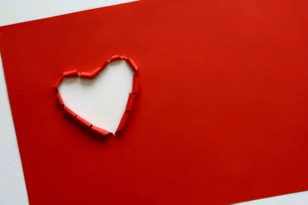 Ripped paper hole heart shaped on red paper background. Valentine\'s day celebration concept