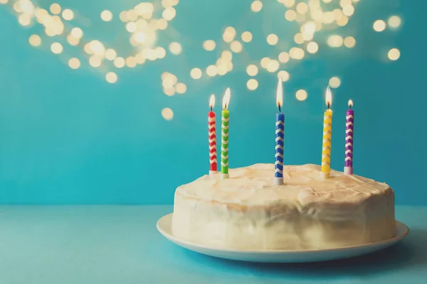 白色生日蛋糕与五颜六色的蜡烛在蓝色背景对脱焦的光 节日庆祝的概念 复制空间 — 图库照片