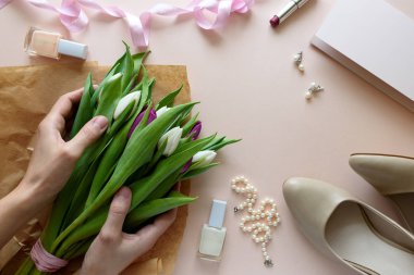 Beyaz ve mor lale buketi holding eller. Kadınsı aksesuarları ve boş kağıt üzerinde pembe bir arka plan. Üstten görünüm. Düz yatıyordu. Uzay kopyalayın. Sevgililer günü, anneler günü, Doğum günü, düğün kutlama kavramı.