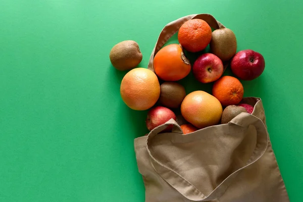 Cotton bag with different fruits on green background. Ecology pack for free plastic shopping. Top view. Flat lay