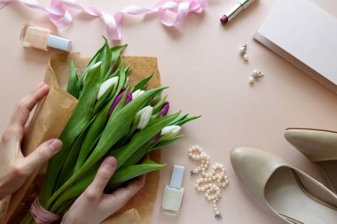 Beyaz ve mor lale buketi holding eller. Kadınsı aksesuarları ve boş kağıt üzerinde pembe bir arka plan. Üstten görünüm. Düz yatıyordu. Uzay kopyalayın. Sevgililer günü, anneler günü, Doğum günü, düğün kutlama kavramı.