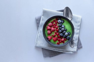 Kahvaltı kivi güler yüzlü kase dondurulmuş ahududu, yaban mersini ve gri ahşap arka plan üzerinde kırmızı kuş üzümü ile zirveye yerleşti. Üstten görünüm. Kopya alanı