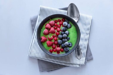 Kahvaltı kivi güler yüzlü kase dondurulmuş ahududu, yaban mersini ve gri ahşap arka plan üzerinde kırmızı kuş üzümü ile zirveye yerleşti. Üstten görünüm. Kopya alanı