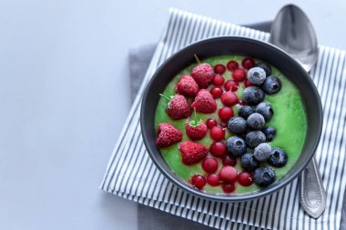 Kahvaltı kivi güler yüzlü kase dondurulmuş ahududu, yaban mersini ve gri ahşap arka plan üzerinde kırmızı kuş üzümü ile zirveye yerleşti. Üstten görünüm. Kopya alanı