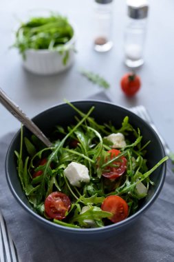 Roka salata domates ve peynirle gri ahşap zemin üzerine kase. Vejetaryen yiyecekler kavramı