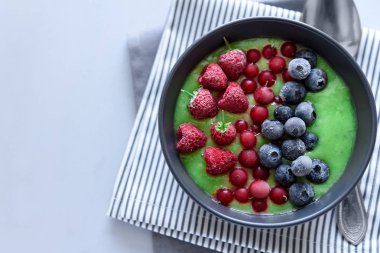 Kahvaltı kivi güler yüzlü kase dondurulmuş ahududu, yaban mersini ve gri ahşap arka plan üzerinde kırmızı kuş üzümü ile zirveye yerleşti. Üstten görünüm. Kopya alanı