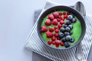 Kahvaltı kivi güler yüzlü kase dondurulmuş ahududu, yaban mersini ve gri ahşap arka plan üzerinde kırmızı kuş üzümü ile zirveye yerleşti. Üstten görünüm. Kopya alanı