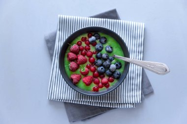 Kahvaltı kivi güler yüzlü kase dondurulmuş ahududu, yaban mersini ve gri ahşap arka plan üzerinde kırmızı kuş üzümü ile zirveye yerleşti. Üstten görünüm. Kopya alanı