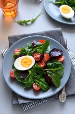Salata karışımı ile ıspanak, roka, pancar yaprakları, domates ve gri ahşap arka plan üzerinde yumurta. Vejetaryen yiyecekler kavramı. Seçici odak.