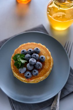 Dondurulmuş yaban mersini ve gri arka plan üzerinde ballı krep yığını. Seçici odak