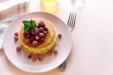 Dondurulmuş ahududu, kırmızı kuş üzümü ve pembe bir arka plan üzerinde ballı krep yığını. Seçici odak