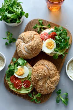 Krem peynir, avokado, domates, yumurta ve Yeşiller gri ahşap zemin üzerine simit sandviç. Seçici odak. Sağlıklı beslenme veya Vejetaryen yiyecekler kavramı