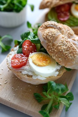 Krem peynir, avokado, domates, yumurta ve Yeşiller gri ahşap zemin üzerine simit sandviç. Seçici odak. Sağlıklı beslenme veya Vejetaryen yiyecekler kavramı