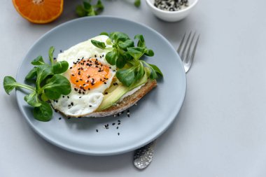 Kızarmış ekmek (sandviç) krem peynir, avokado, yumurta ve yeşillik gri ahşap zemin üzerinde. Seçici odak. Sağlıklı beslenme veya Vejetaryen yiyecekler kavramı